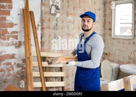 Mann, der Holzmaterialien auf der Baustelle trägt Stockfoto