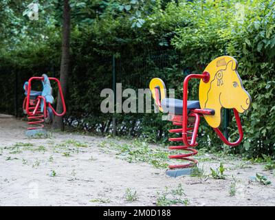 Gelbe Pferde und blaue Motorradschaukel auf einem sandig grünen Vorort Spielplatz Stockfoto