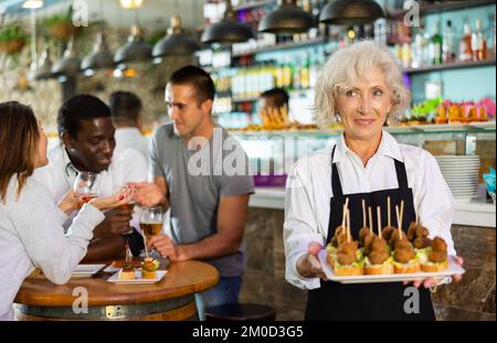 Blick auf die europäische ältere Frau, die an einer Bar Pinchos hält Stockfoto
