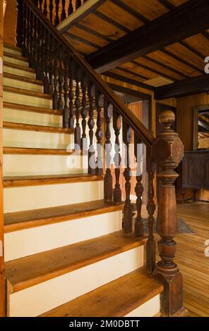 Kiefernholztreppen mit umgewandeltem neuen Pfosten und Geländer, die zum oberen Stockwerk in einem alten Haus im 1826-Kanadiana-Cottage-Stil führen. Stockfoto