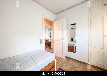 Ein Schlafzimmer mit antiken weißen Holzmöbeln, einem Einzelbett, einem Spiegel an der Wand und einem eingebauten Kleiderschrank Stockfoto