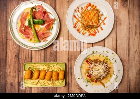 Ein Set köstlicher Rezepte mediterraner Gastronomie mit Böhmen und Hühnchen-Kroketten, iberischer Seife mit Eiern und Kartoffeln auf einem Holztisch Stockfoto