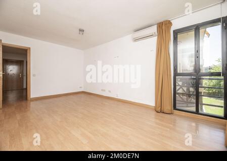 Leeres Wohnzimmer eines Hauses mit hellbraunem Laminatboden, Erkerfenster mit schwarz eloxierten Aluminiumfenstern und hellbraunen Vorhängen Stockfoto
