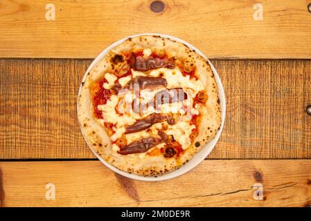 Tolle italienische Pizza mit dünner Kruste und gebratenen Speckstreifen mit Mozzarella-Käse und Tomaten, die in einem Steinofen gebacken wurden Stockfoto