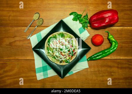 Ein Salat mit Gemüse und viel Soße auf einem Pizzabrot auf einem schwarzen Teller Stockfoto