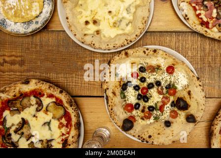 Set italienischer Pizzas mit dünner Kruste mit schwarzen Oliven, Kirschtomaten, getrocknetem Oregano, Basilikum, Auberginenscheiben, pomodoro-Tomate und viel Käse zum Auftragen Stockfoto