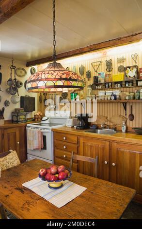 Küche mit Retro-Herd und antikem Tisch, Theke und Gewürzgläser auf Regalen im alten Haus im kanadischen Landhausstil um 1810. Stockfoto