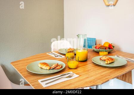 Ein faltbarer Esstisch aus Bambusholz mit flachen und tiefen Tellern und Gläsern gefüllt mit Orangensaft und frischem Obst Stockfoto