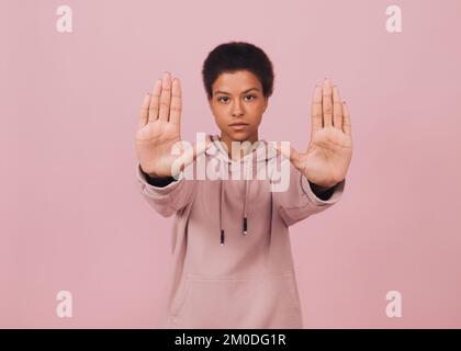 Ein echtes schwarzes Mädchen, das mit Stoppgesten steht. Junge Afro-Frau mit Warnzeichen auf rosa Hintergrund Stockfoto