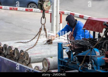 Ein Arbeiter befestigt Ketten von einem Kran an Betonrohren auf dem Laderaum eines LKW Stockfoto