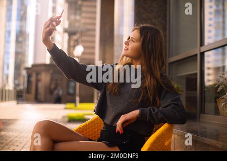 Eine städtische Frau nimmt Selfies mit ihrem Handy, während sie in einem Café sitzt, Hände bei der Arbeit mit digitaler Technologie Stockfoto