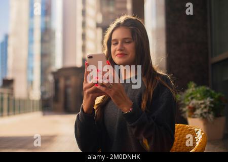 Urban Casual Woman Generation Z überprüft ihr Telefon im Sitzen in einem Café, Hände bei der Arbeit mit digitaler Technologie Stockfoto