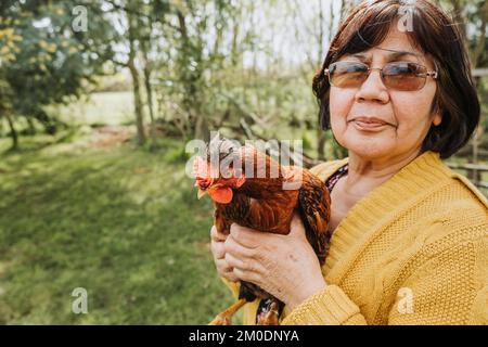 Nahaufnahme einer lateinamerikanischen Farmerin mit roter Hühnerrasse in einer ländlichen Landschaft. Speicherplatz kopieren Stockfoto
