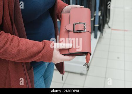 Schwangere Frau in einem Geschäft sucht sich eine rote Unterarmtasche zum Kauf aus. Die Hände schließen sich Stockfoto