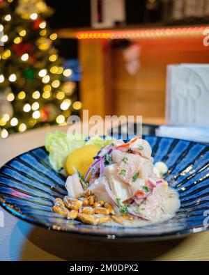Peruanische Ceviche wird auf einem blauen Teller serviert, mit Weihnachtslichtern im Hintergrund Stockfoto