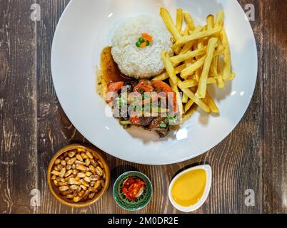 lomo-Saltado mit weißem Reis und pommes frites, serviert auf einem Holztisch - 3.RAF Stockfoto