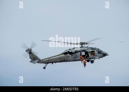 221117-N-EV253-1710 SAN DIEGO (17. Nov. 2022) – US Naval Aircewmen (Helicopter) arbeiten zusammen mit Vertretern von Air Rescue Systems (ARS) daran, Personal in einen MH-60s Seahawk Helikopter zu befördern, der den „Merlins“ der Helicopter Sea Combat Squadron (HSC) 3 im Rahmen eines dynamischen Proof Concept-Kurses zugewiesen wurde. Der Kurs, der von dem Leiter des Such- und Rettungsmodells (SARMM) des HSC-3 geleitet wurde, wurde konzipiert, um Navy-Piloten und -Besatzungen die Physik hinter dem Anheben von Hubschraubern und neue Techniken zu vermitteln, um sichere und effiziente dynamische Hebevorrichtungen durchzuführen. Sonstiges Stockfoto