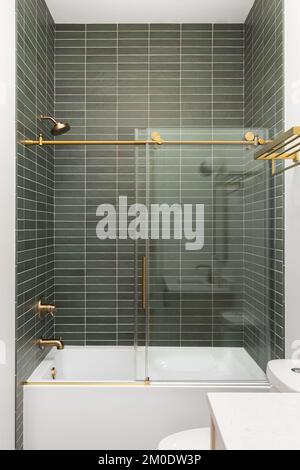 Eine Dusche mit grünen Subway-Fliesen, goldenem Wasserhahn und Akzenten sowie eine weiße Badewanne. Stockfoto