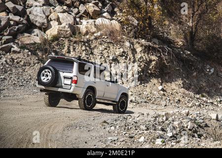 Weißer SUV, der das bergige felsige Gelände hinunterfährt Stockfoto