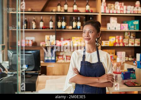 Porträt einer lächelnden jungen Frau, die an der Ladentheke steht und wegschaut Stockfoto