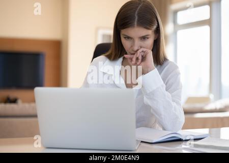 Eine seriöse, aufmerksame, freiberufliche Mitarbeiterin, die zu Hause am Arbeitsplatz sitzt Stockfoto