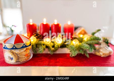 Weihnachtsgebäck und vier brennende Kerzen auf einem Adventskranz, schöne Dekoration, die auf die traditionellen Feierlichkeiten wartet Stockfoto