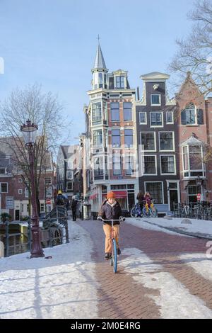 Amsterdam Niederlande 2021. Februar, ein kalter Wintertag mit einer Frau auf einem Fahrrad in Amsterdam bei Schneewetter Stockfoto