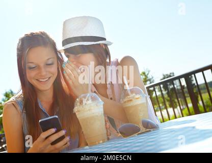 Hast du gehört, Wie Ein Teenager auf einem Handy SMS schreibt, während ihr Freund ihr etwas ins Ohr flüstert? Stockfoto