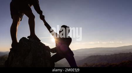 Silhouette der helfenden Hand zwischen zwei Kletterern. Ein paar Wanderungen helfen sich gegenseitig bei der Silhouette in den Bergen mit Sonnenlicht. Die Männer, die helfen, Leute hochzuziehen Stockfoto