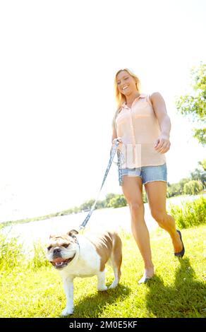 Frische Luft schnappen und Sport treiben. Eine schöne Blondine, die mit ihrem Hund spazieren geht. Stockfoto