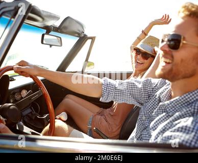 Ich fühle mich so frei. Ein glückliches junges Paar, das an einem schönen Sommertag in einem Cabrio fährt. Stockfoto