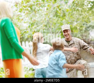 Es ist so schön, zu Hause zu sein. Ein Vater, der von der Armee nach Hause kommt und seine Familie begrüßt, die zu ihm läuft. Stockfoto