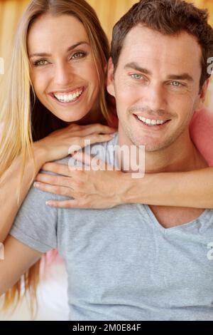 Er gehört mir. Ein glückliches junges Paar, das auf der Couch sitzt und sich liebevoll umarmt. Stockfoto