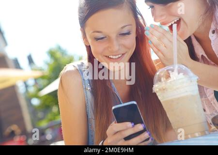 Wenn Gerüchte verbreitet werden... Eine Teenagerin, die auf einem Handy SMS schreibt, während ihr Freund ihr etwas ins Ohr flüstert. Stockfoto