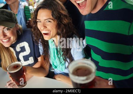 Ich liebe Bier am Sportabend. Eine atemberaubende junge Frau, die ein Bier mit Freunden an der Bar genießt. Stockfoto