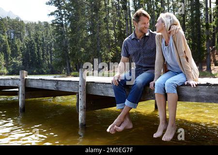 Lachen am See. Ein liebevolles, reifes Paar, das auf einem Pier auf dem Land an einem See sitzt. Stockfoto