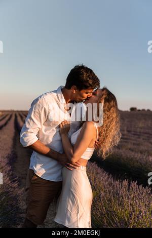Vertikales Foto einer romantischen Szene eines Paares, das sich während des Sonnenuntergangs in einem Lavendelfeld küsst Stockfoto