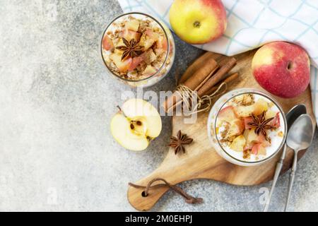 Gesundes Frühstücksgranola, gesunder Lebensstil. Hausgemachtes Dessert mit Joghurt, Müsli, Karamelläpfeln und Zimt auf einem Steintisch. Blick von oben. Co Stockfoto