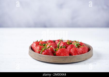 Frische rote Erdbeeren auf einer grauen Keramikplatte auf einem weißen Holztisch. Horizontal, Kopierbereich, Nahaufnahme. Stockfoto