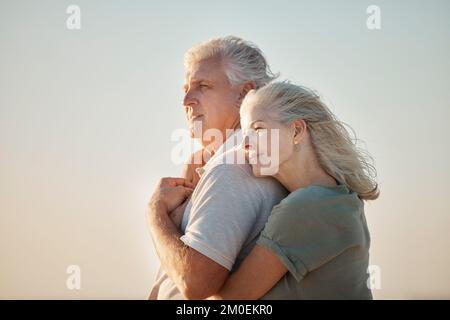 Ein Paar, das am Strand umarmt. Reifes Paar, das den Blick auf den Strand genießt. Seniorenpaar, das sich am Strand anfreundet. Reifes Paar mit Zuneigung Stockfoto