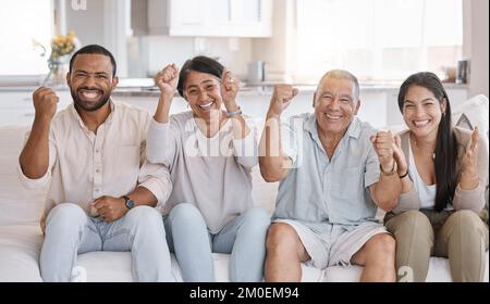 Familienfeiern mit gemischten Rassen, die auf dem Sofa in der Lounge zu Hause sitzen. Die hispanische Familie sieht im Wohnzimmer ekstatisch aus Stockfoto