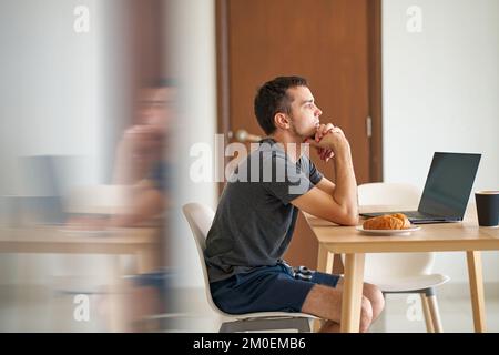 Der Typ war angespannt zu denken, als er die Nachrichten las, während er an seinem Laptop saß. Stockfoto