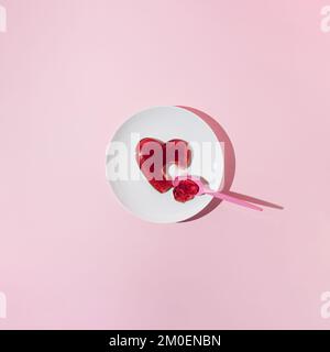 Rotes Gelee-Herz mit Kunststofflöffel auf weißem Teller. Liebe oder Valentinstag Minimalkonzept. Stockfoto