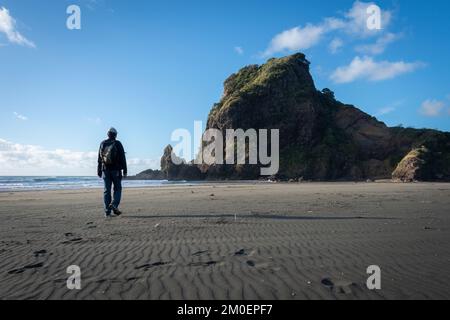 Ein Mann geht in Richtung des Löwenfelsens am Piha Beach, blauer sonniger Tag. Waitakere, Auckland. Stockfoto