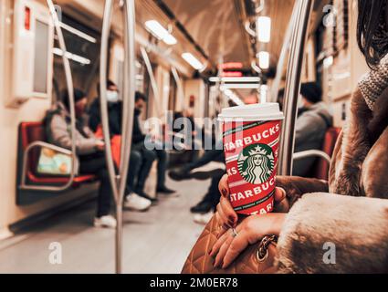 Eine Nahaufnahme einer Frau, die in der U-Bahn sitzt und eine Tasse Starbucks-Kaffee hält Stockfoto