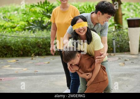 Glückliche dreiköpfige Familie, die Verstecken im Stadtpark spielt Stockfoto