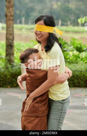 Der kleine Junge umarmt seine Mutter mit verbundenen Augen, wenn sie Verstecken spielen Stockfoto