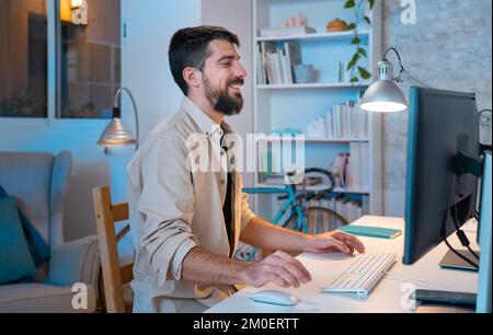 Junger kreativer Unternehmer, der zu Hause in seinem modernen Arbeitsbereich mit einem Lächeln arbeitet. Stockfoto