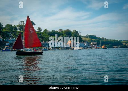 22. Juli 2021 - Fowey, Großbritannien: Eine Bootsfahrt um den Hafen von Fowey und das markante rote Segel auf einem vorbeifahrenden kleinen Boot. Stockfoto