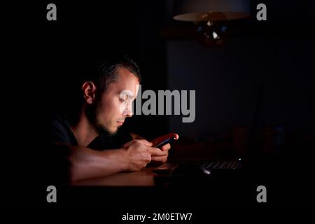 Ein Typ im Dunkeln, der die Nachrichten auf seinem Handy liest. Stockfoto